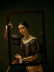 Portrait of a girl wearing a princess or countess dress over dark studio. portrait through picture...