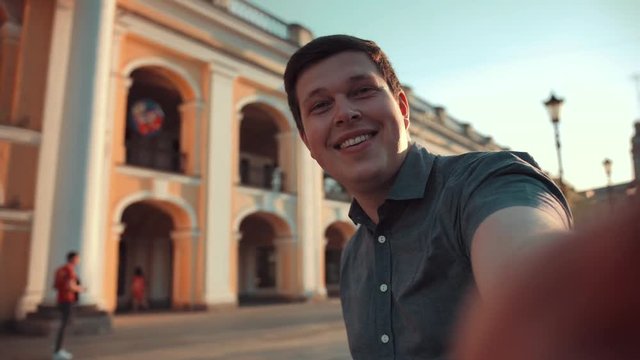 POV wide view of happy man doing selfies on smartphone in the city. Smiling and laughing good holiday mood.