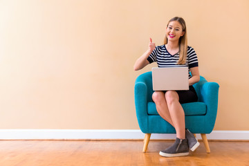 Young woman with a laptop computer giving thumb up in a chair