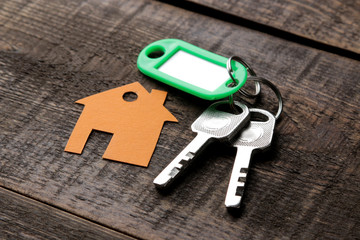 The concept of buying a home. Keys with a keychain and a house on a brown wooden background.