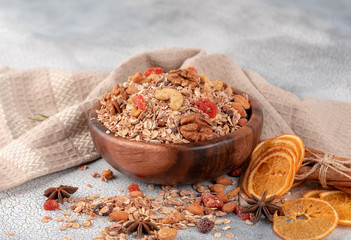 Wooden Bowl with granola with nuts, dried cranberries and dried orange on a old light table