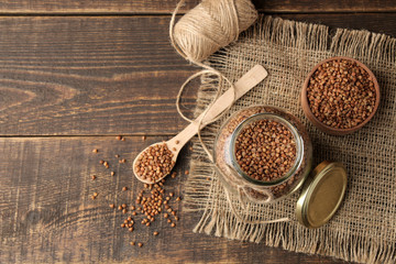 Dry buckwheat groats in a glass jar with a wooden spoon. top view on wooden brown table. cereals. healthy food. porridge.