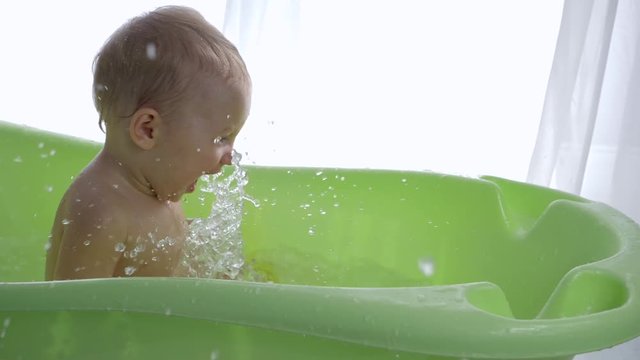 funny Games, cheerful infant boy delight splashing water while taking bath close-up