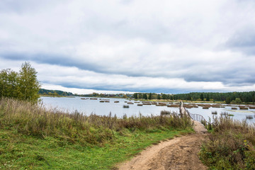 Autumn landscape with a long pedestrian bridge and a cloudy sky.