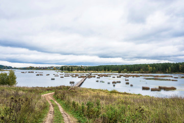 Autumn landscape with a long pedestrian bridge and a cloudy sky.