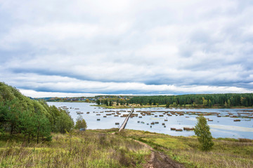 Autumn landscape with a long pedestrian bridge and a cloudy sky.