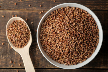 Dry buckwheat groats in a white bowl with a spoon on a wooden brown table. cereals. healthy food. porridge. top view