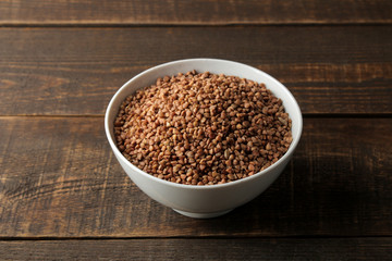 Dry buckwheat groats in a white bowl on a wooden brown table. cereals. healthy food. porridge.