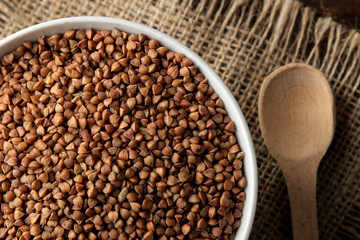 Dry buckwheat groats in a white bowl with a spoon on a wooden brown table. cereals. healthy food. porridge. top view