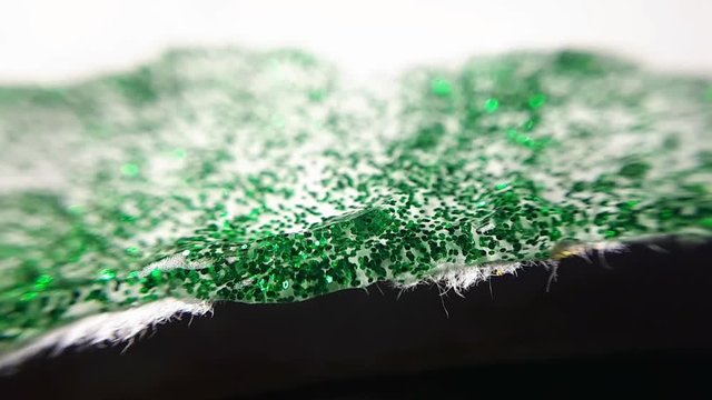 Green Wet Glitter On a Uneven Edge Of Paper. Macro Close Up Shot.