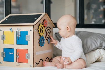 A child is playing with a wooden house. A special model of a house with many functions for the development of fine motor skills. Busy Board. - obrazy, fototapety, plakaty