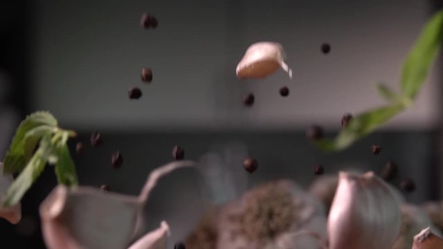 Garlic falling with pepper and leaves to wood cutting board, on kitchen background. Slow motion 240 fps. Sony rx 10