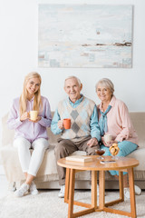 young woman sitting on sofa and drinking tea with senior parents