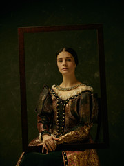Portrait of a girl wearing a princess or countess dress over dark studio. portrait through picture...