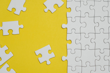 Fototapeta premium Fragment of a folded white jigsaw puzzle and a pile of uncombed puzzle elements against the background of a yellow surface.