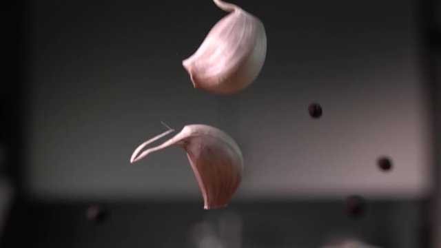 Garlic falling with pepper and leaves to wood cutting board, on kitchen background. Slow motion 480 fps. Sony rx 10