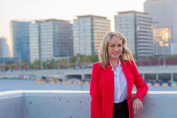 Fototapeta premium Blonde woman wearing red jacket and black shirt standing in the city