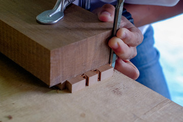 Skilled joiner working in carpentry. Amateur woodworker making dovetail join for wooden drawer in carpenters workshop