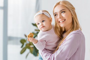 young mother holding small cute daughter with cookie