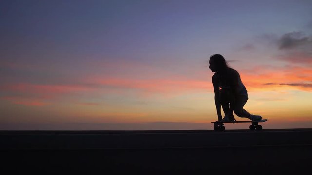 Beautiful girl rides a skateboard on the road against the sunset sky