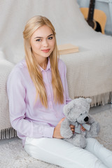 attractive woman sitting on carpet with teddy bear in hands