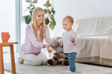 young woman with little daughter playing toys on carpet