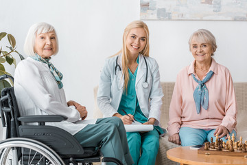 Obraz premium young female nurse sitting on sofa and writing prescription to senior women
