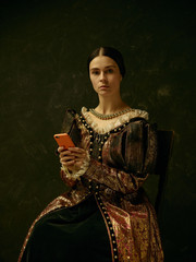 Portrait of a girl wearing a princess or countess dress with mobile phone over dark studio making...