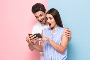 Image of attractive couple 20s smiling and looking at mobile phone, isolated over colorful...
