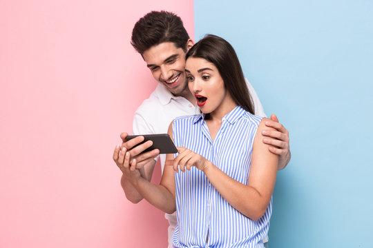 Image of joyful couple 20s smiling and looking at mobile phone, isolated over colorful background