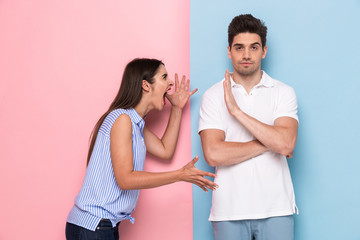Photo of crazy woman in casual clothes yelling at man standing face to face, isolated over colorful...