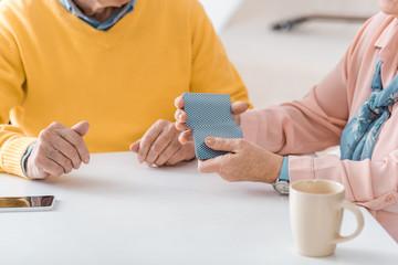 close up of senior people playing cards on white table