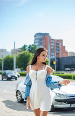 Attractive pretty woman in white dress with jeans jacket looking at camera while standing on street