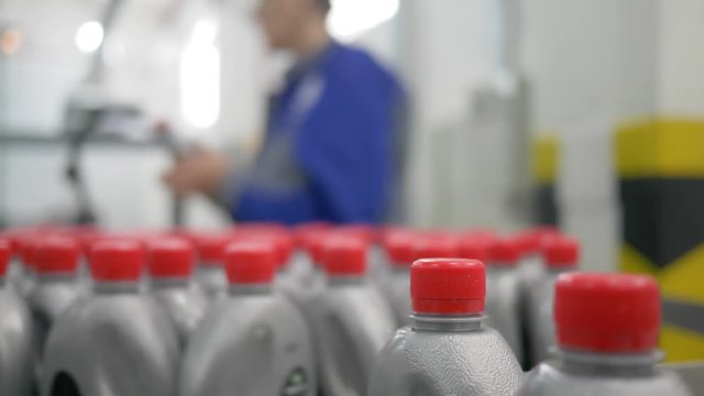 machine oil factory, plastic bottles in grey with red lids move in a circle on conveyor belt indoors near the worker