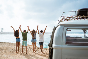 Happy friends walking at beach and rise up hands