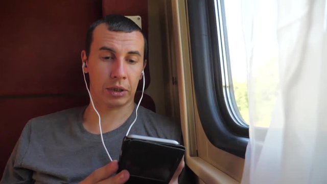 man listening to the music on the train rail car coupe compartment travel. slow motion video. man with a smartphone at lifestyle the window of a train in a car travel internet social media web. man