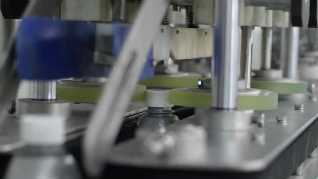 plant of engine oils, automatic machine closes caps on grey plastic bottles on conveyor line close up