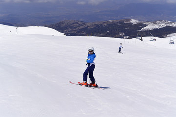 A boy in ski suit, helmet and sunglasses skiing from snowy mountains in Serra Nevada