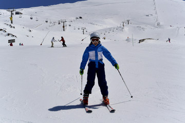 Fototapeta na wymiar A boy in ski suit, helmet and sunglasses skiing from snowy mountains in Serra Nevada