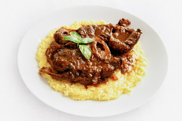 beef shank braised with wine and vegetables, garnished with risotto, and decorated with basil