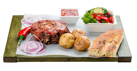 Set of pork steak, vegetable salad, potatoes and sauce. On a wooden board. Chalagach.