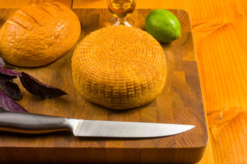 national Adyghe cheese homemade on a cutting Board with a knife, Basil, parsley, lime, sesame oil,...
