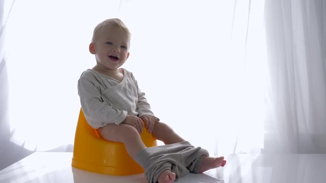 children hygiene, happy infant sitting on potty and smiles in bright room close-up