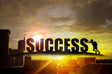 Silhouette of kid pushing the alphabet "success" on the building at sunset
