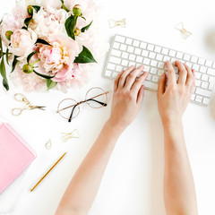 Flat lay women's office desk. Female workspace with female hands, computer, pink peonies bouquet,...
