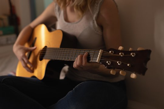 Woman playing guitar in bedroom at home