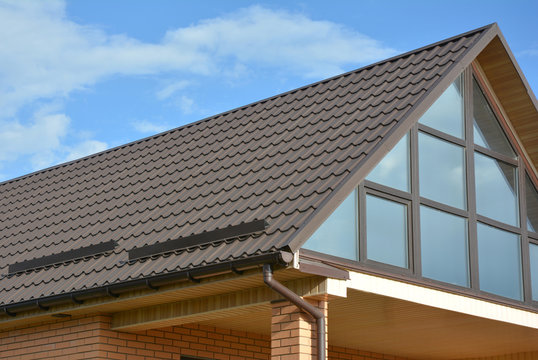 Modern house attic  metal tile roof with panoramic glass wall window and roof gutter.