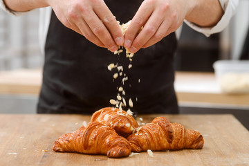Baker sprinkles croissants with almond