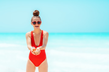 happy young woman on seacoast showing sea shell