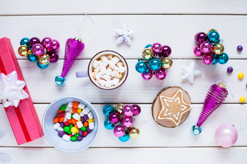 Cup of chocolate with marshmallows, gingerbread cookies, gifts and beautiful Christmas decorations on the white wooden background. Flat lay, top view, space for a text. Close up.